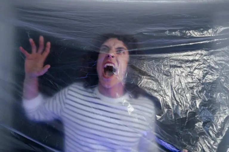 Man in striped shirt screaming behind translucent plastic conveying fear.