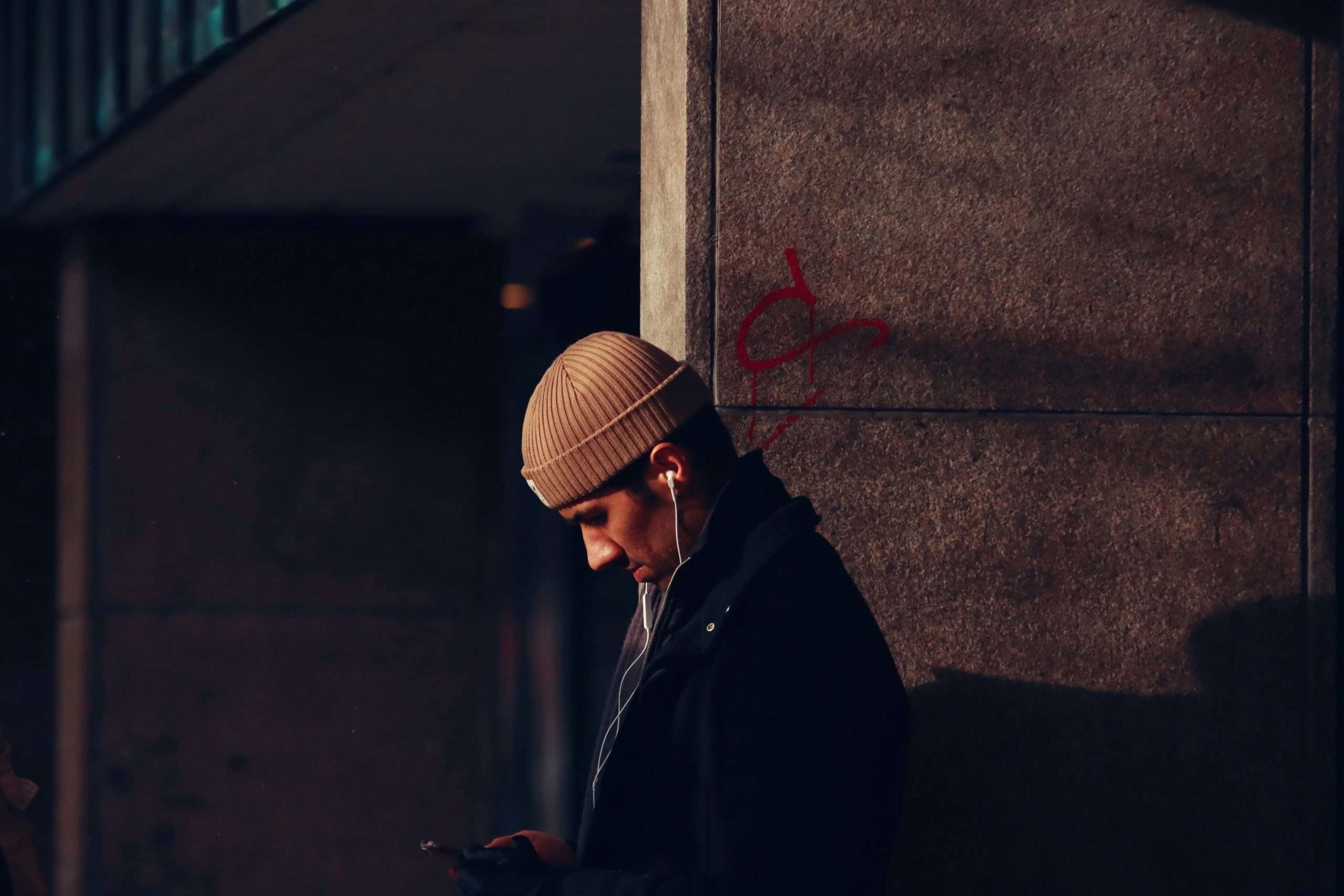 Solitary figure in beanie listening to music against urban brick wall
