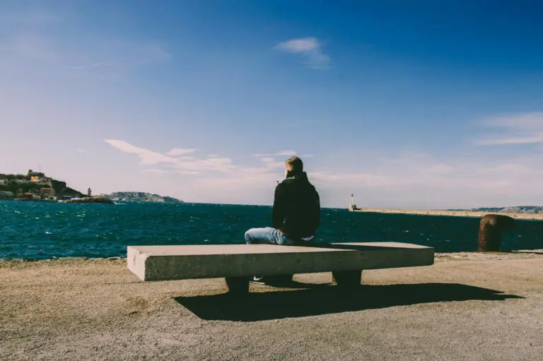 Man sits alone on bench by coastline in marseille, tranquil sea and sky blend.
