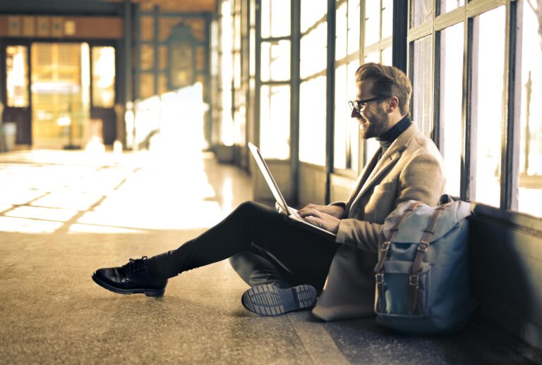 Man working on laptop by sunlit window at Budapest train station.