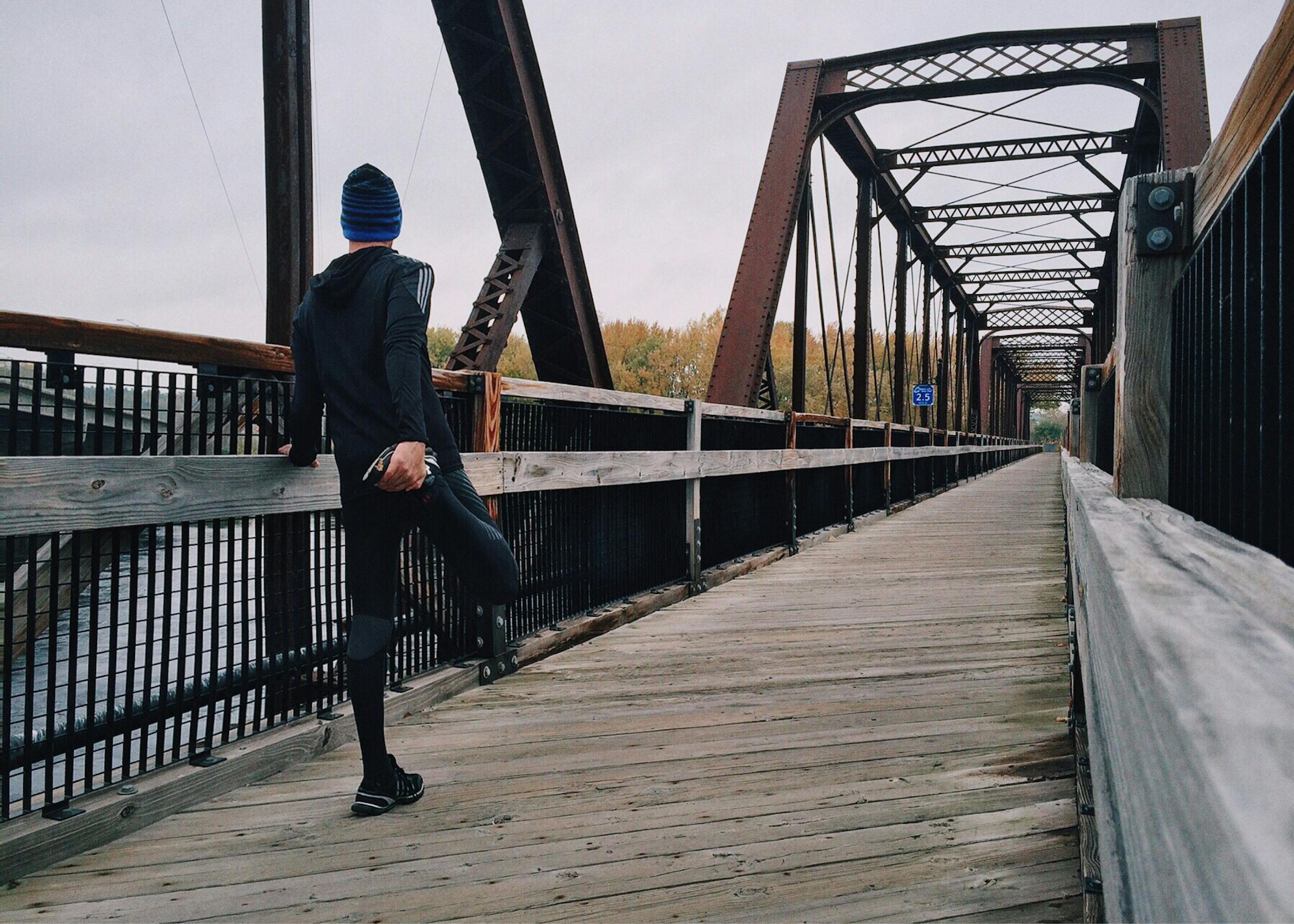 Man stretching on wooden footbridge during daytime run emphasizing fitness recreation