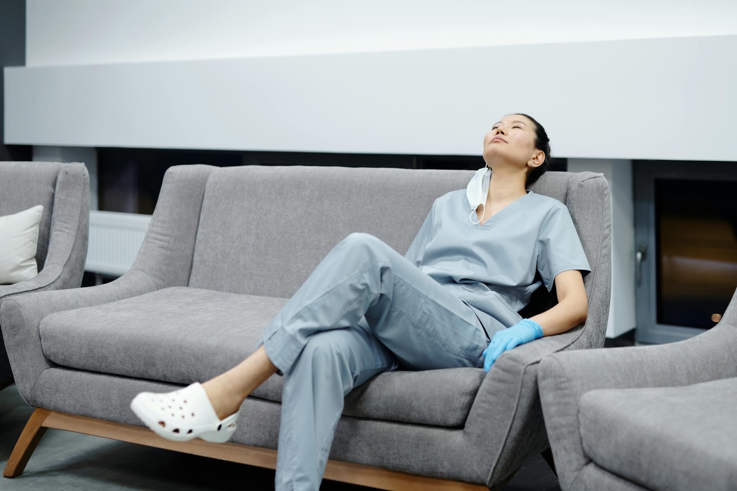 Healthcare worker in scrubs resting on hospital couch after exhausting shift