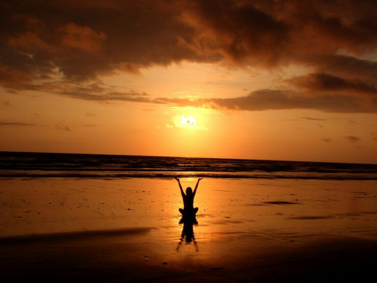 Silhouette of person meditating peacefully at sunset on serene beach.