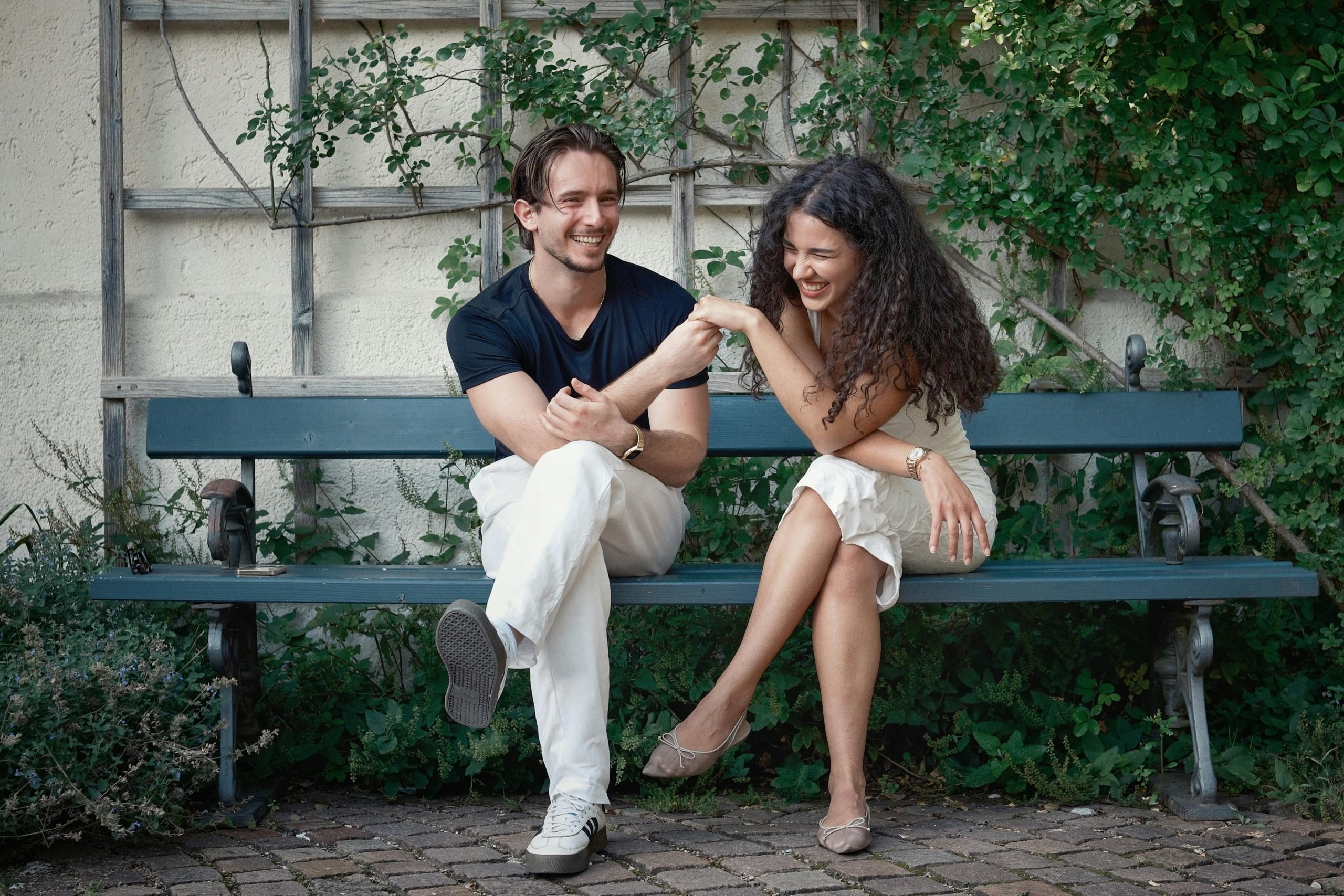Two young adults sitting together on bench, smiling and enjoying meaningful conversation outdoors.