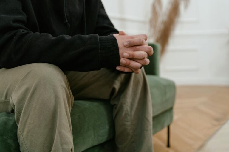 Person sitting thoughtfully in comfortable therapy waiting room with soft lighting and calming decor