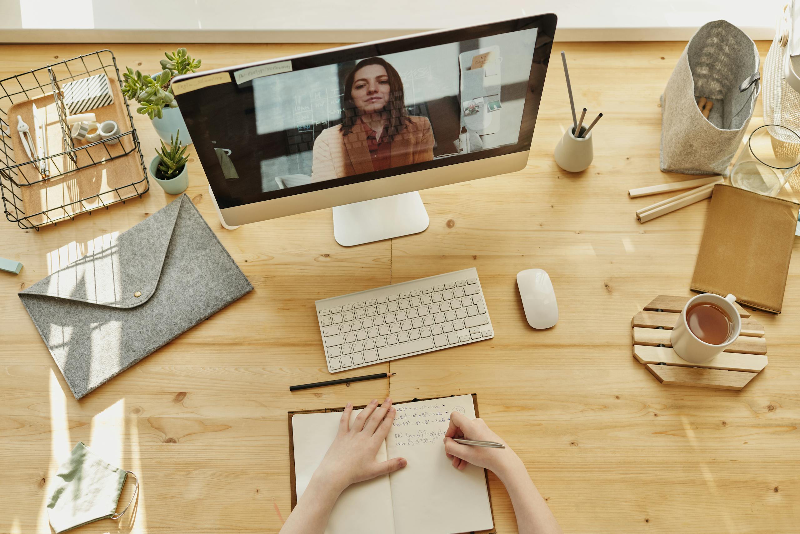 Person taking notes during video call at organized home desk
