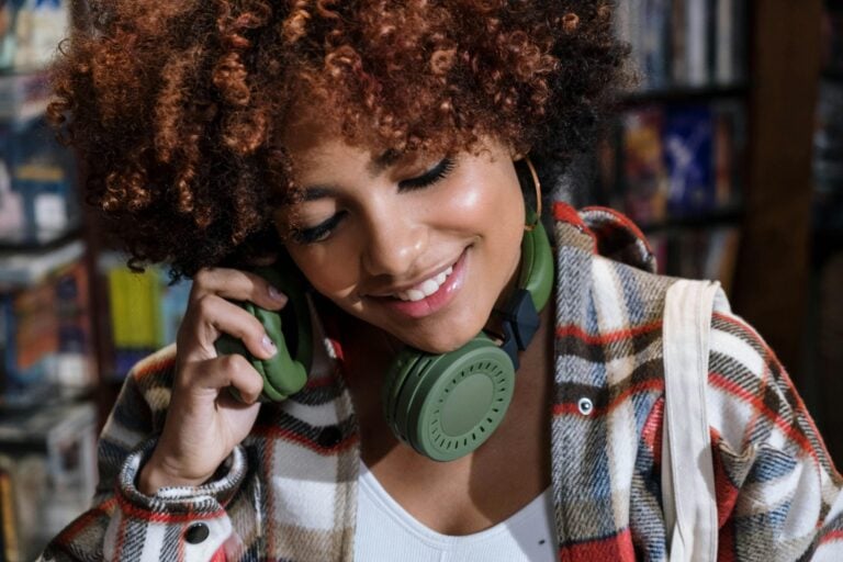 Young woman with curly hair wearing green headphones, smiling peacefully while listening to music