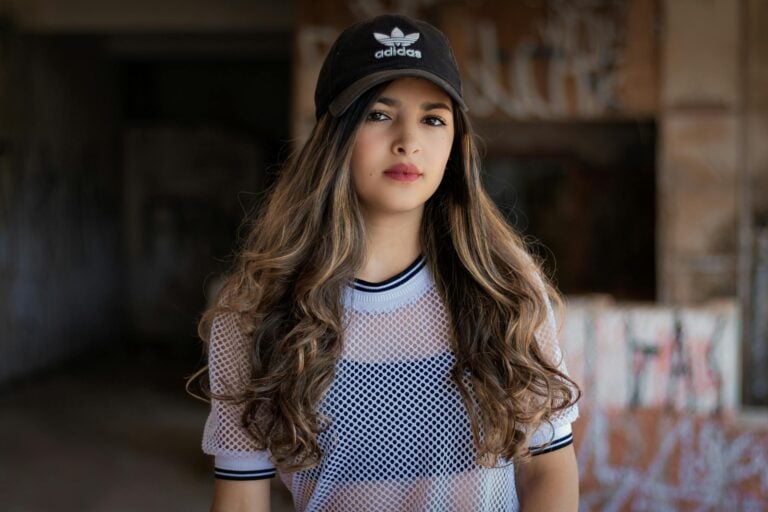 Portrait of young woman wearing Adidas cap and white mesh top.