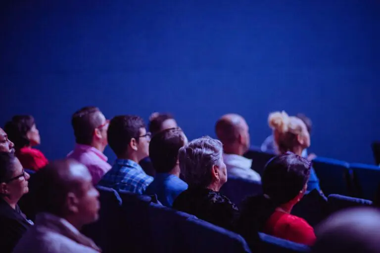 Group of diverse people sitting together in blue-lit theater, watching performance