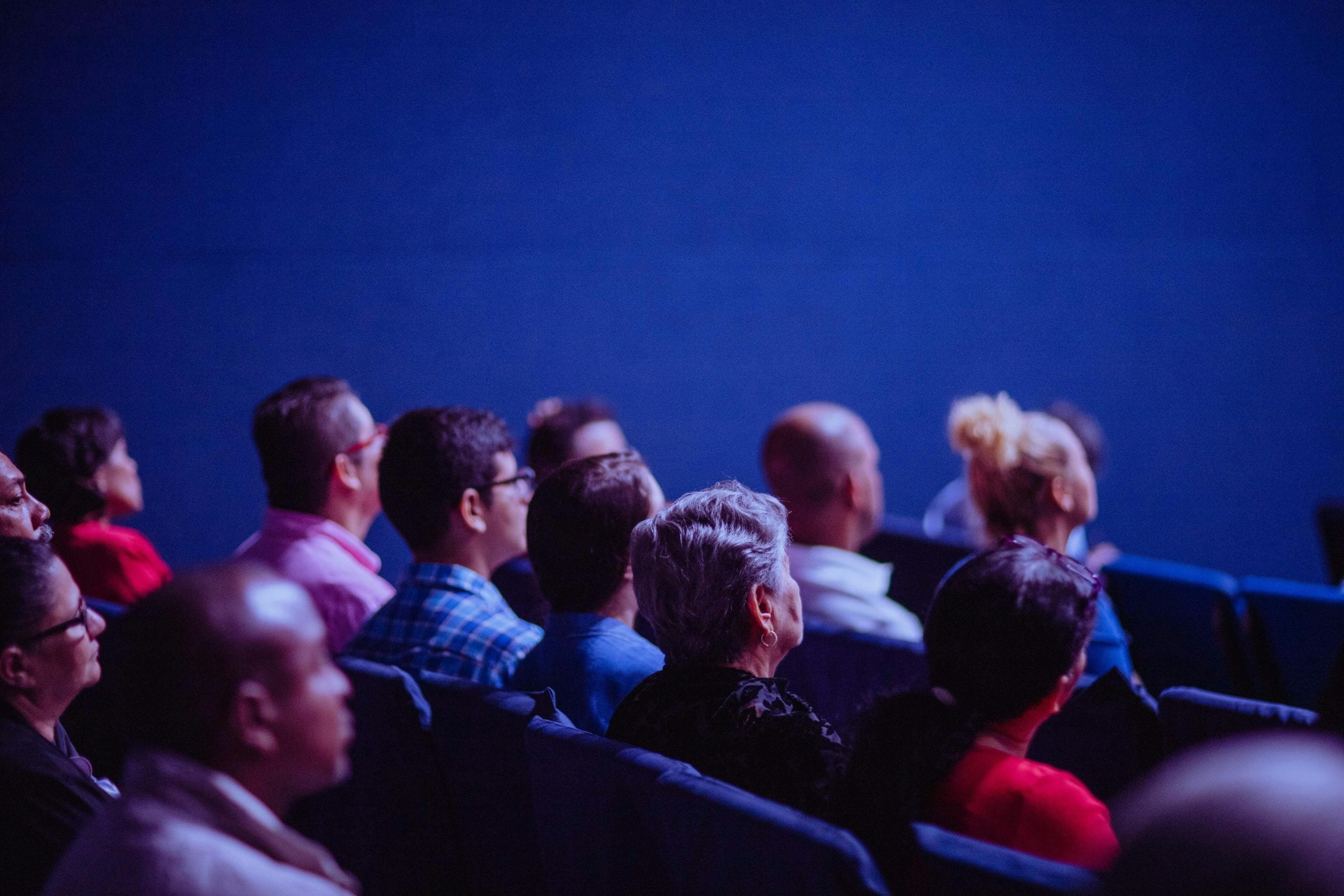 Group of diverse people sitting together in blue-lit theater, watching performance