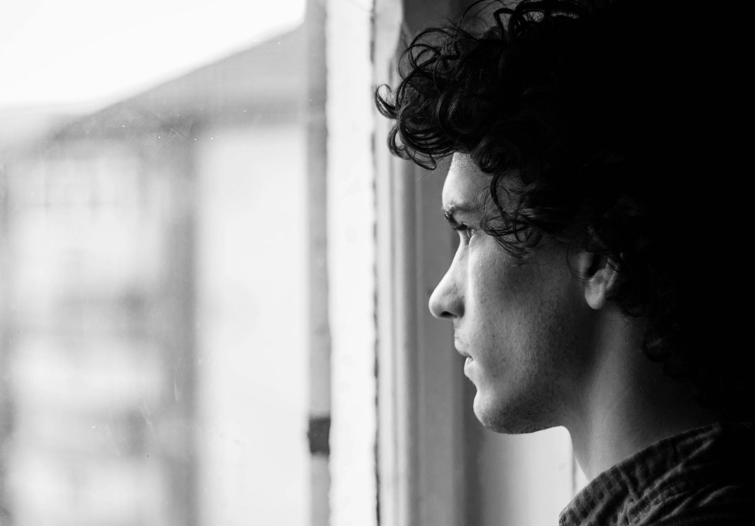 Young man in profile looking thoughtfully out window in black and white