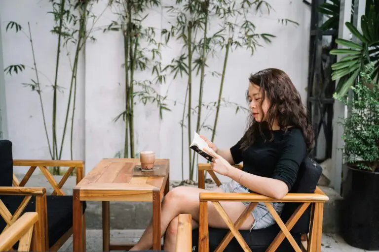 Woman alone at wooden table checking phone in serene garden setting