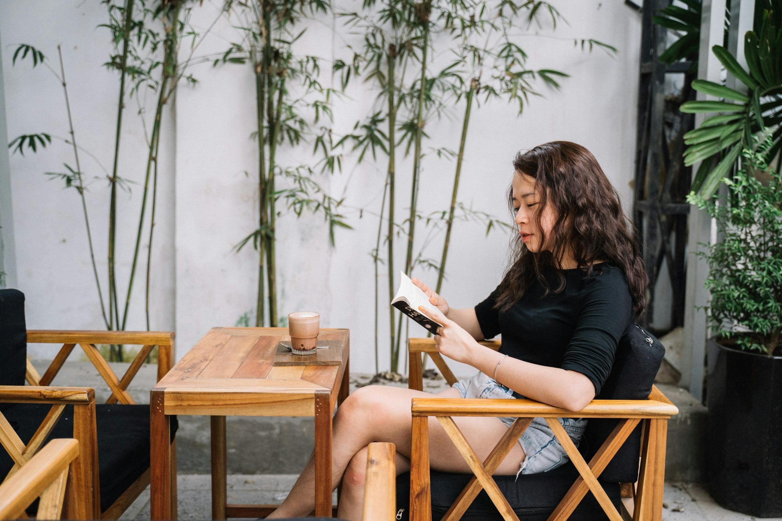 Woman alone at wooden table checking phone in serene garden setting