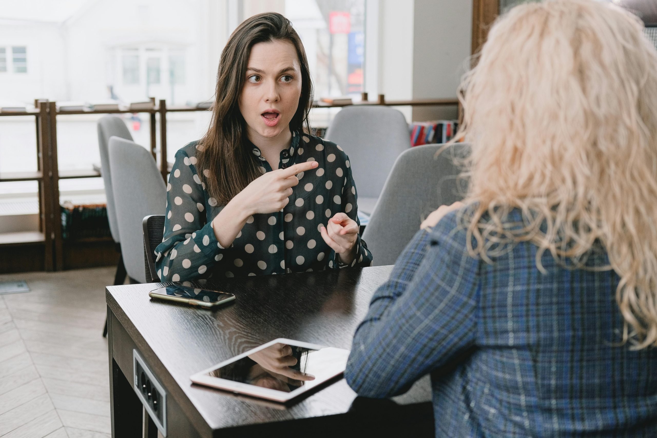 Two women in professional conversation at desk in modern office setting