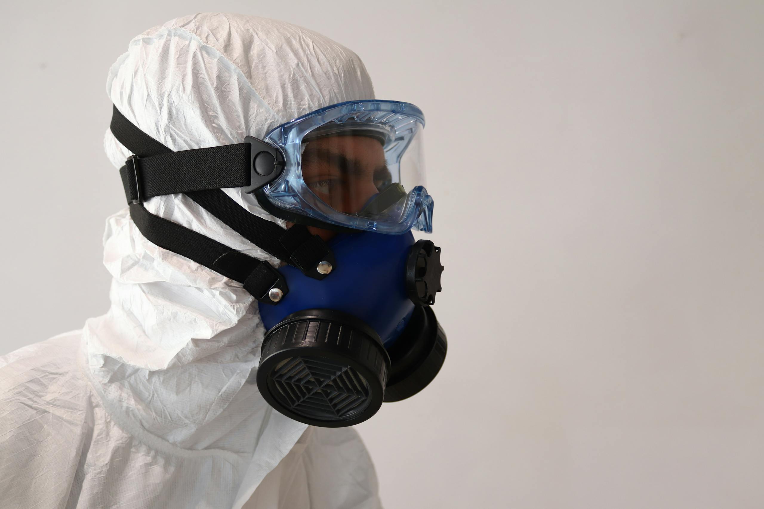 Person in protective suit wearing gas mask against white background