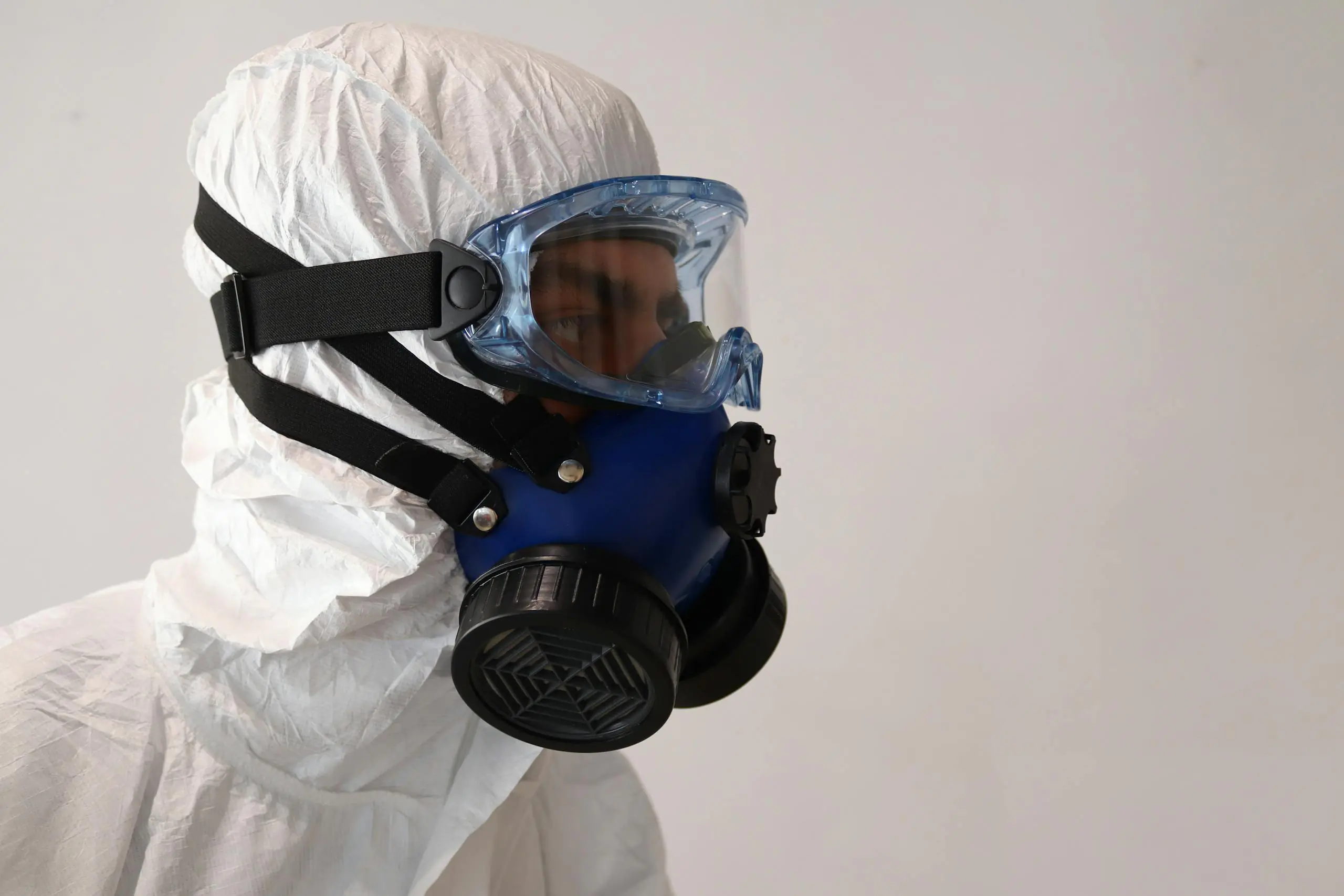 Person in protective suit wearing gas mask against white background