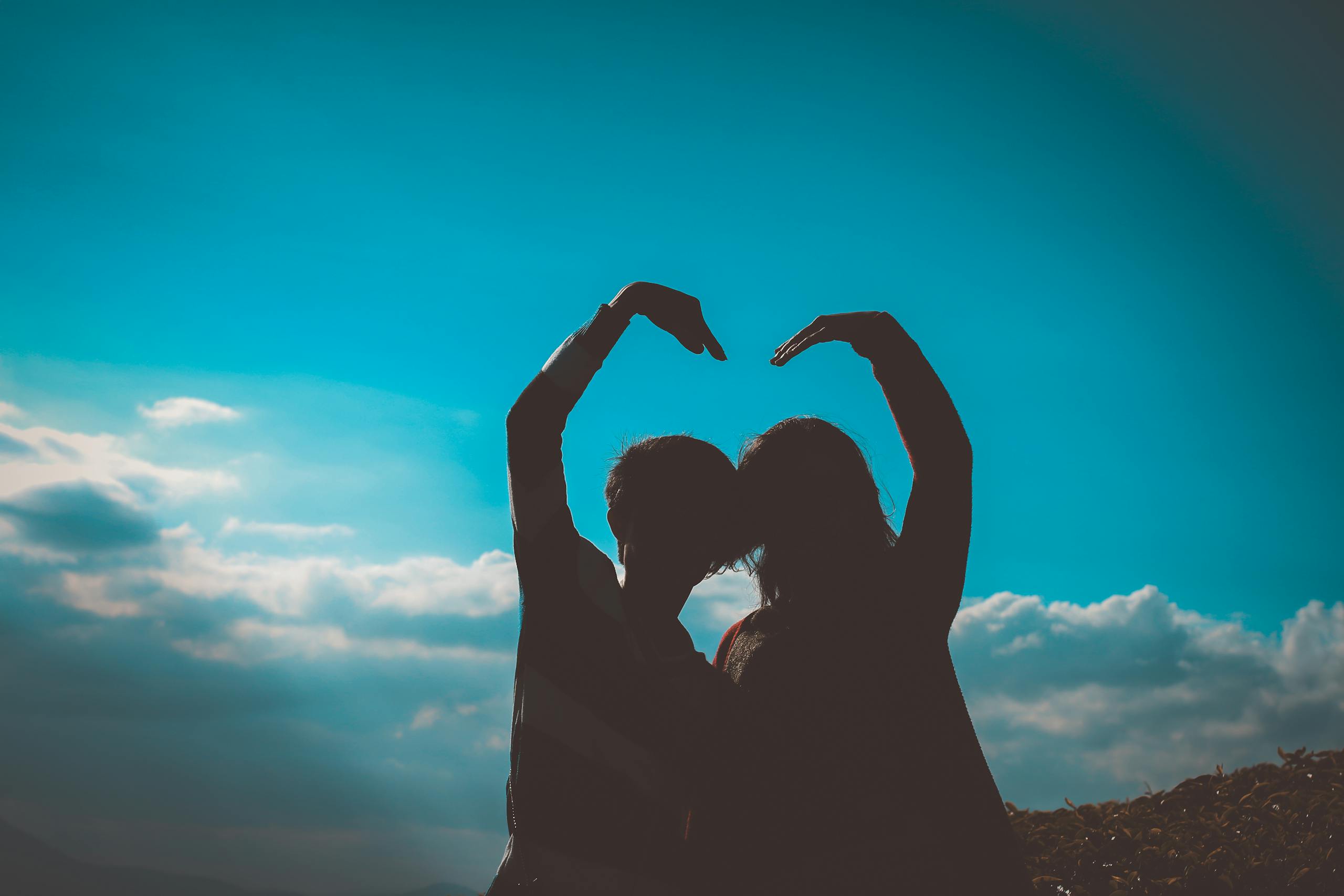 Silhouette of couple creating heart shape with arms in romantic outdoor setting.