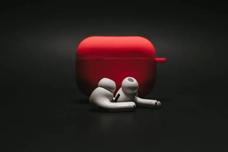 Sleek white earbuds with modern red case on dark surface stylishly.