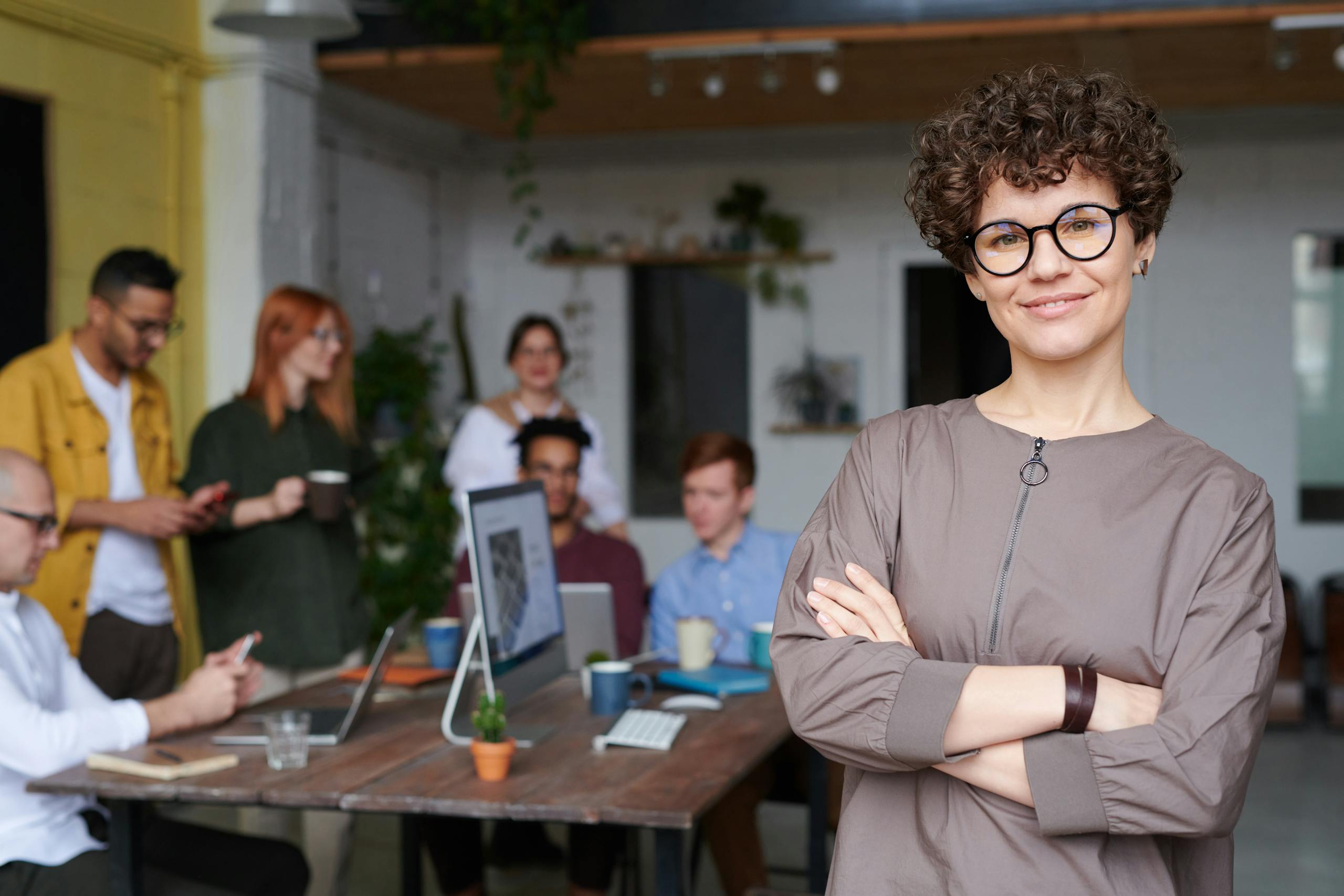 Smiling businesswoman with curly hair standing confidently in modern office.