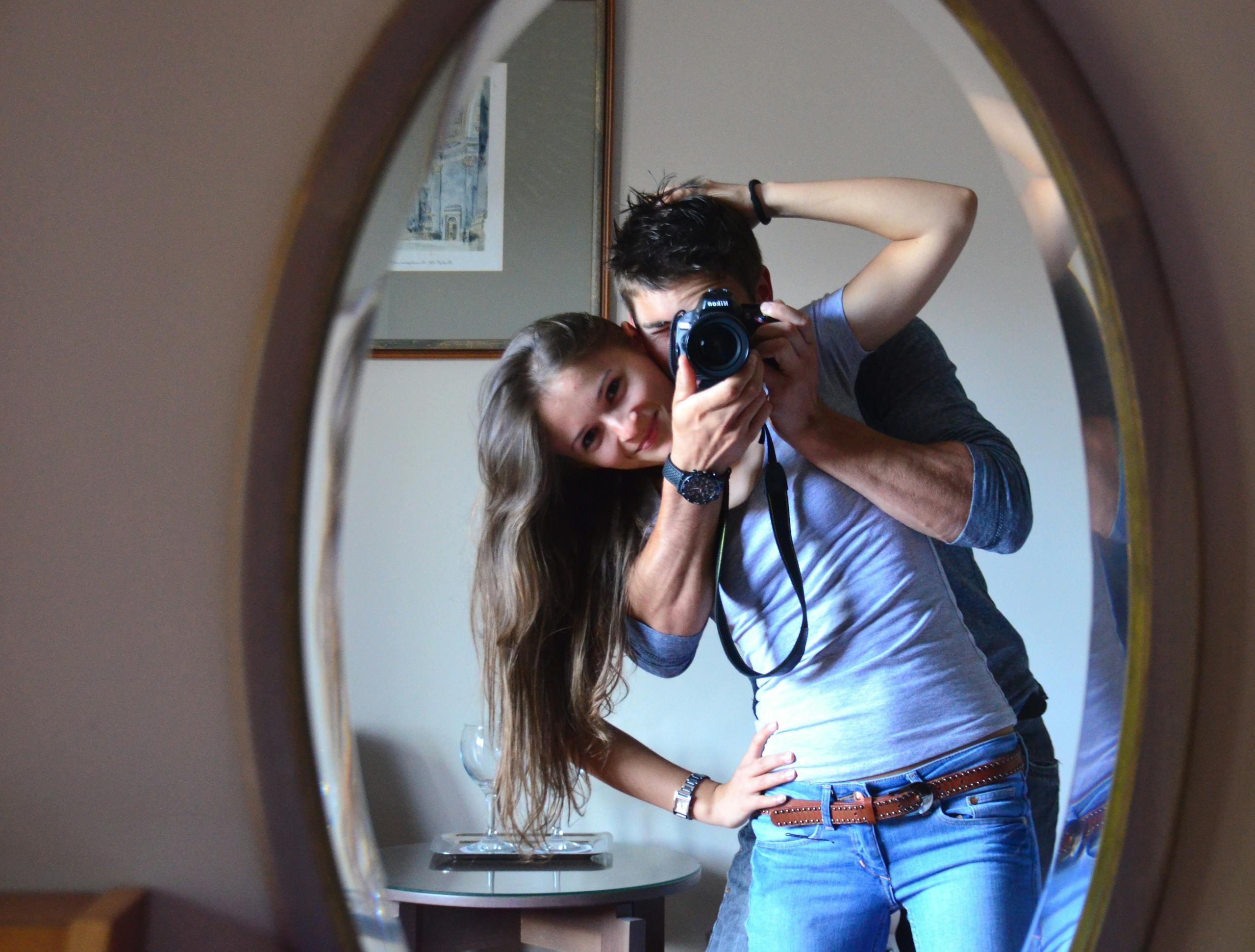 Smiling couple capturing joyful moment with mirror selfie indoors together.