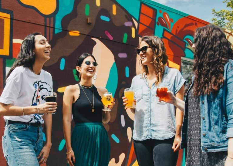 Four diverse women enjoying beverages together against vibrant street art mural
