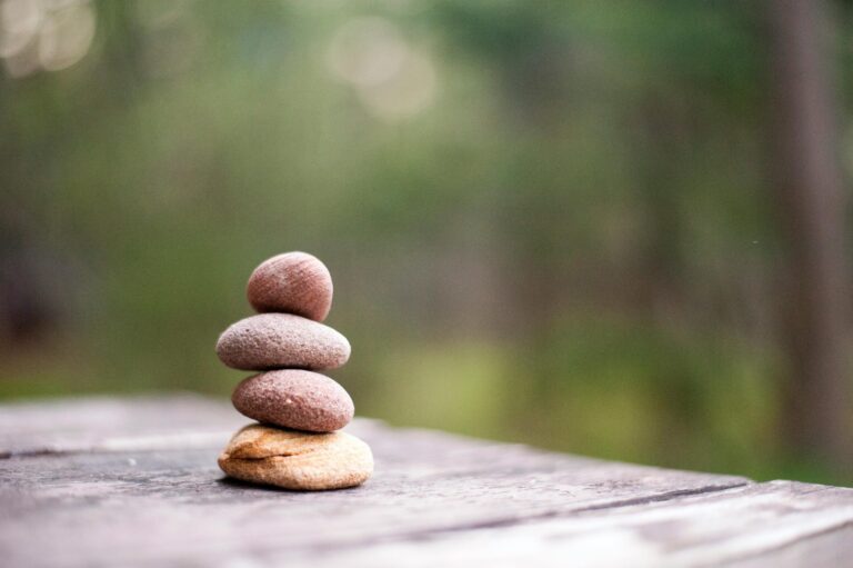 Stacked pebbles balanced carefully on wooden surface with blurred green nature background