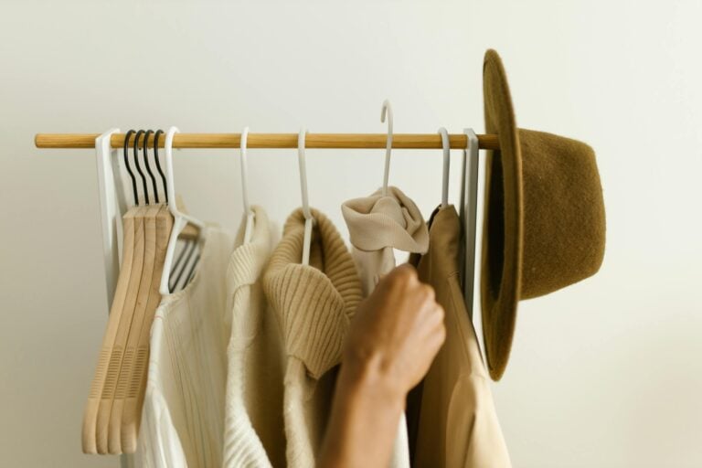 Stylish beige and brown clothes on retail rack with hand selecting item