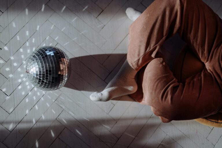 Person in brown clothing gazes at disco ball casting light patterns indoors