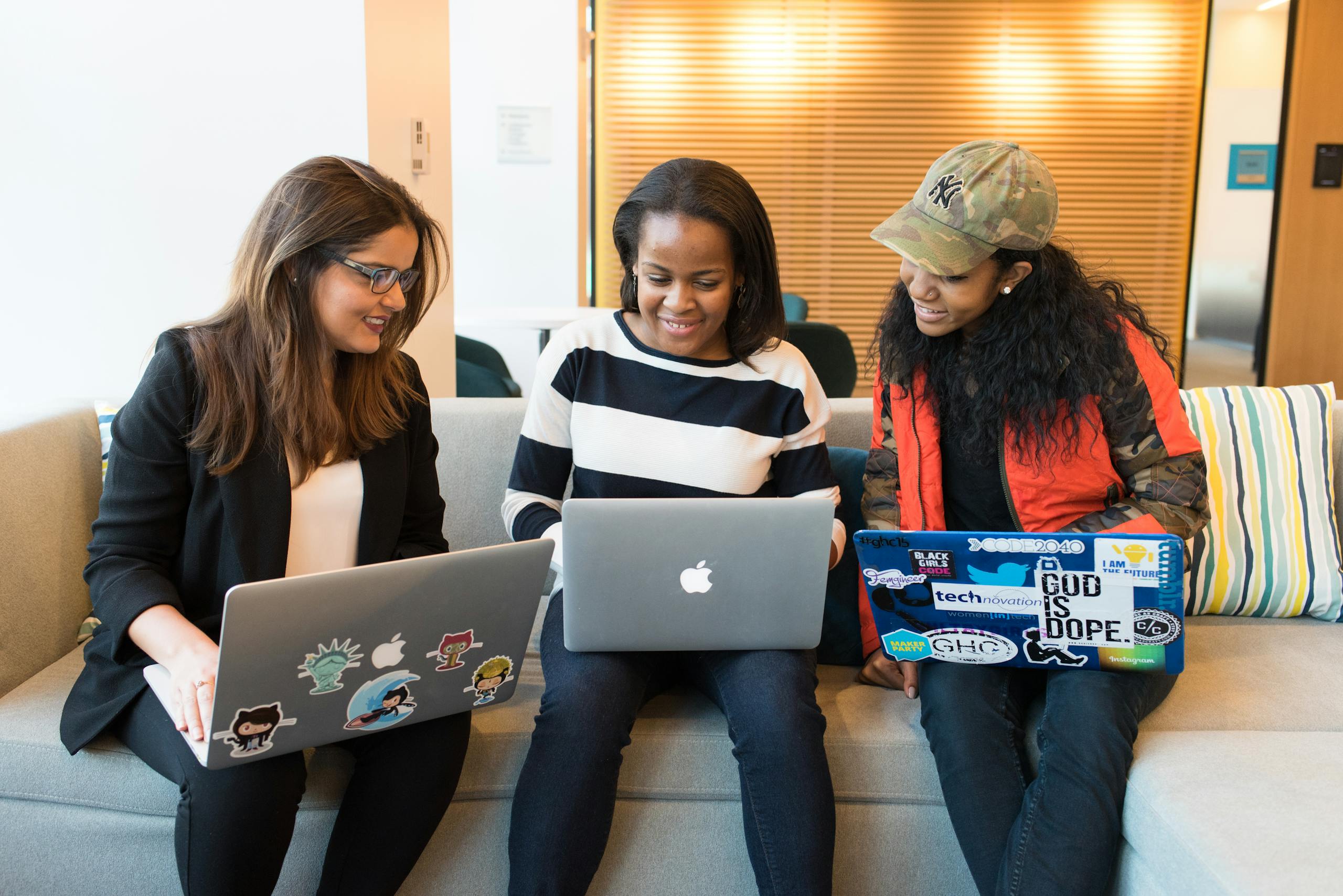 Three women working together on laptops in casual office setting emphasizing teamwork.