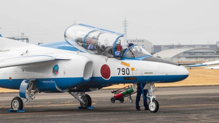 Training jet with Japanese insignia taxiing on airfield runway.
