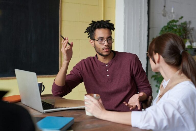 Two colleagues engaged in discussion during team meeting at office table