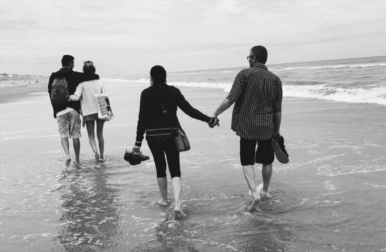 Two couples walking hand in hand on sandy beach with gentle waves