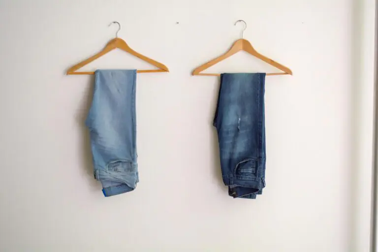 Two pairs of blue denim jeans hanging neatly on wooden hangers