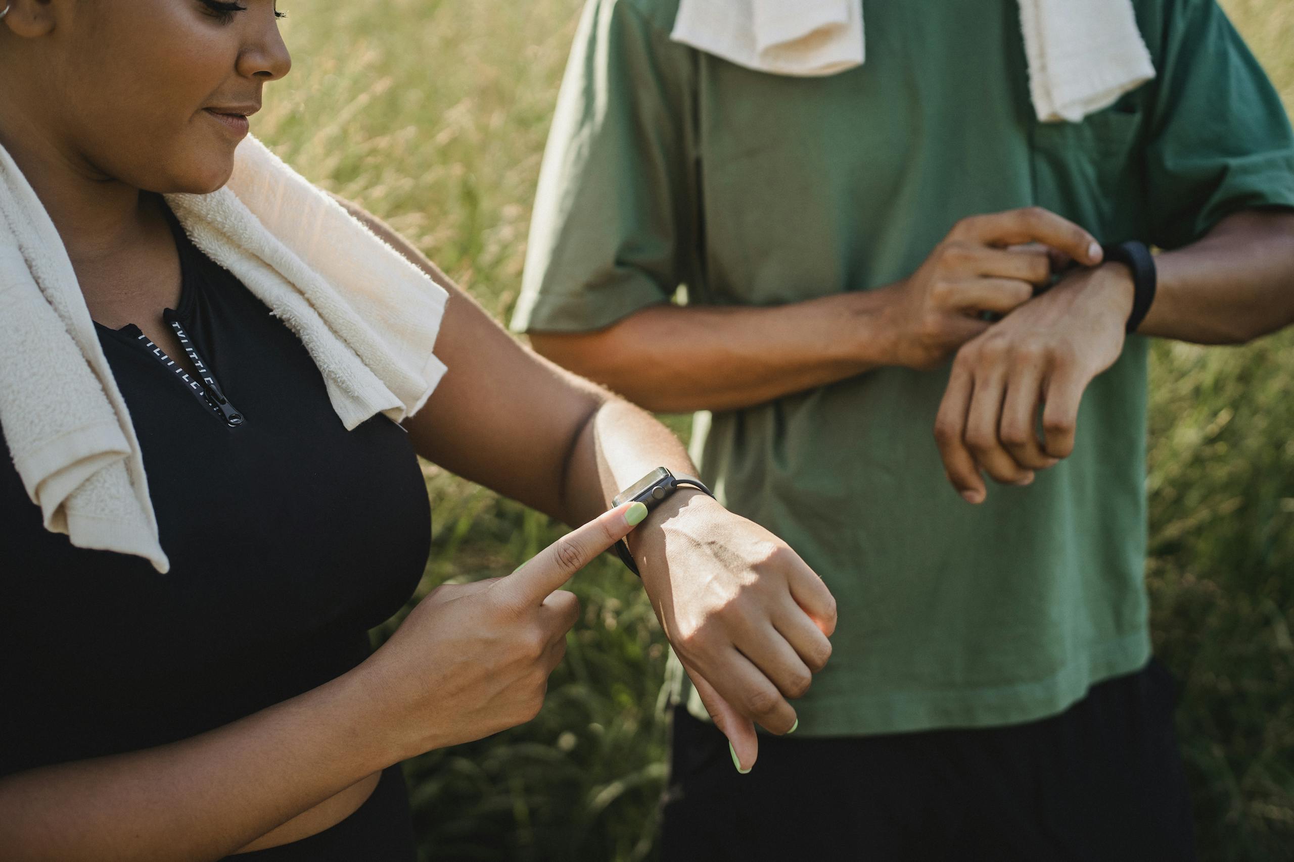 Two people checking fitness watches while taking workout break outdoors