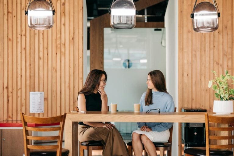 Two women chatting over coffee in stylish indoor cafe setting