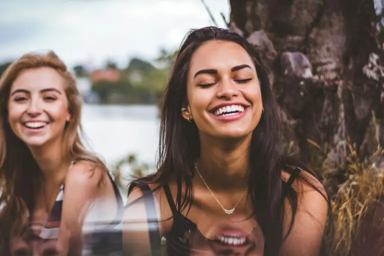 Two women happily laughing together outdoors by serene lakeside