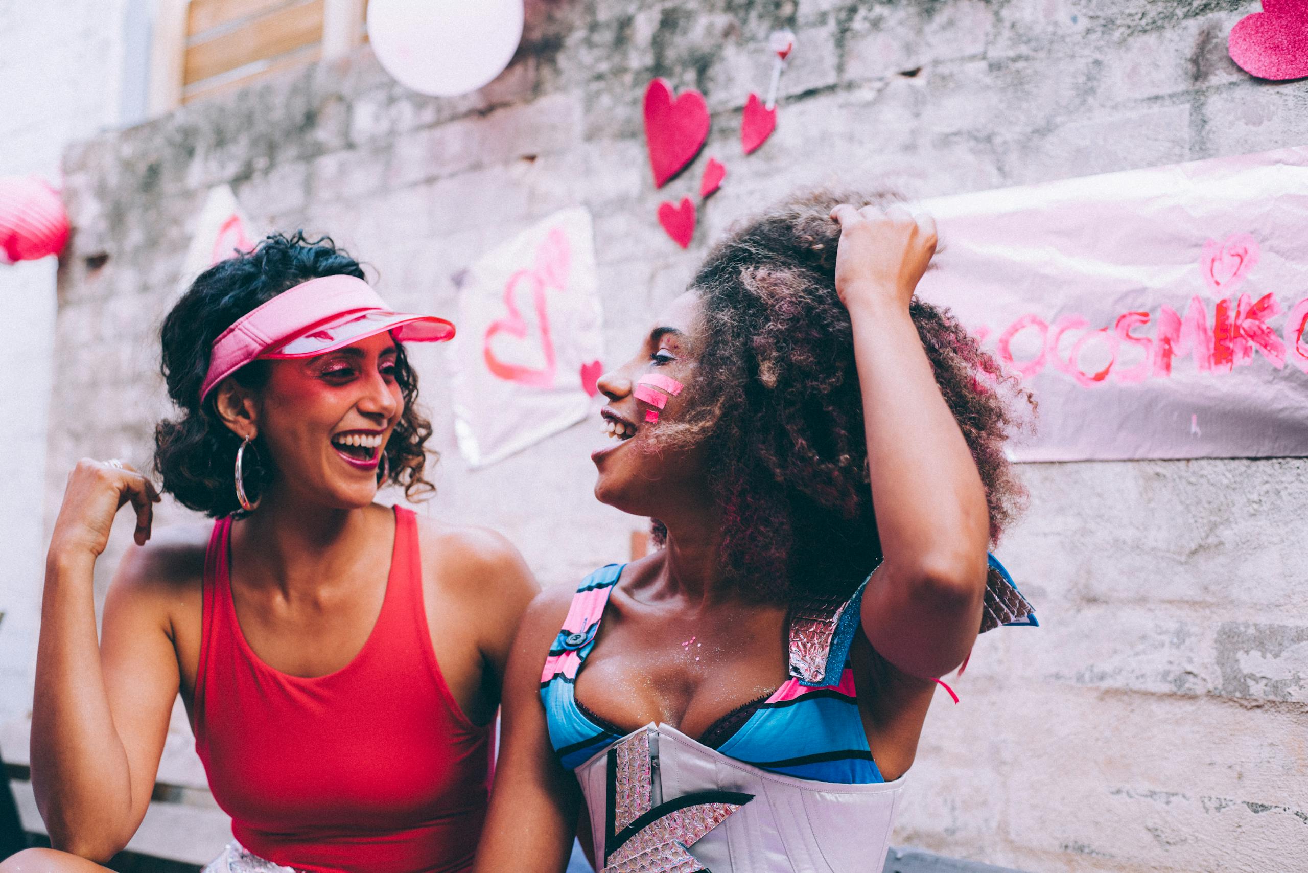 Two women laughing together at colorful outdoor celebration with heart decorations.