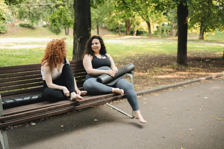 Two women sitting on park bench chatting after yoga session together.