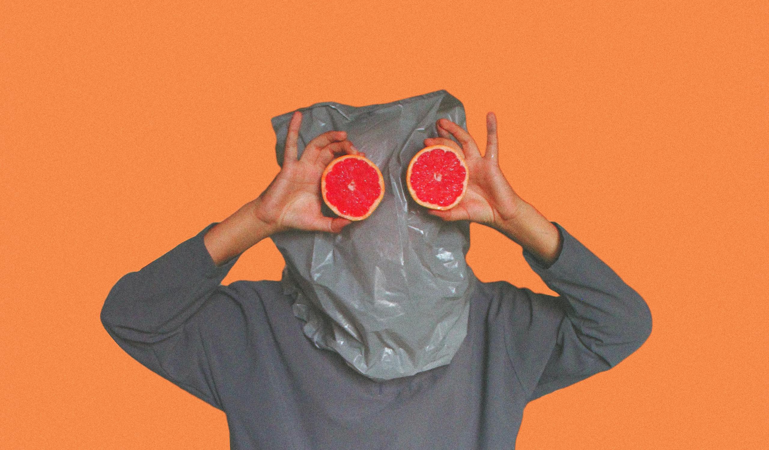 Whimsical portrait with grapefruit slices held in front of face playfully.