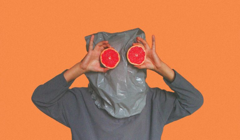 Whimsical portrait with grapefruit slices held in front of face playfully.