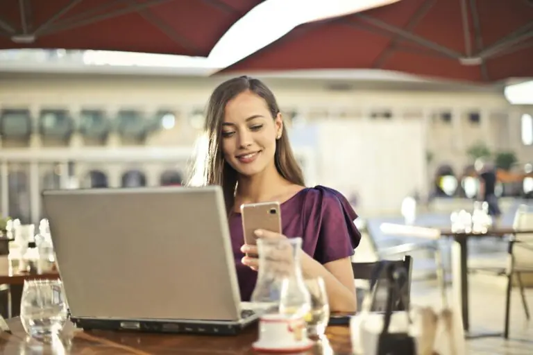 Woman enjoying remote work at cafe with laptop and smartphone present.