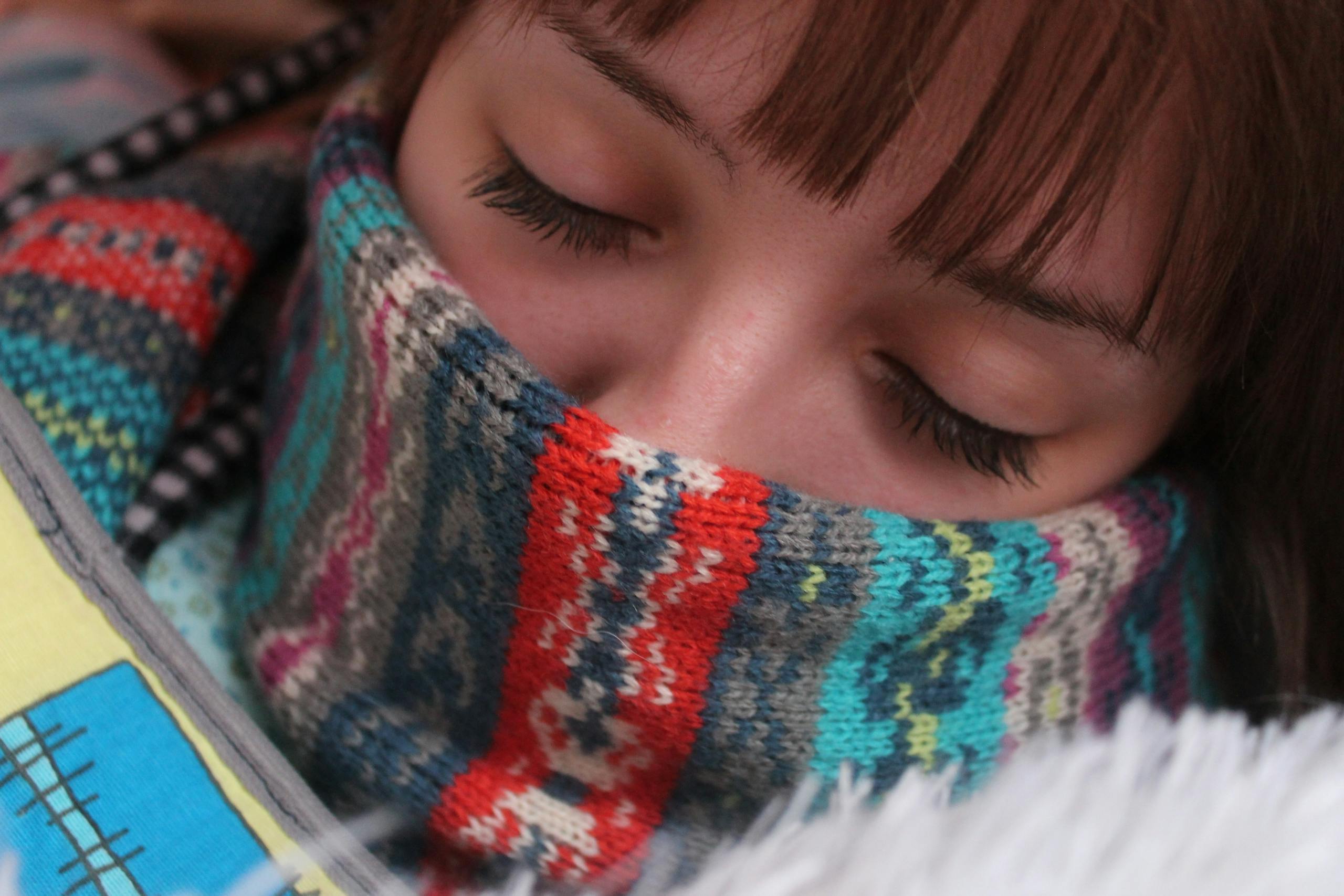 Woman resting with eyes closed wrapped in warm colorful wool scarf depicting comfort