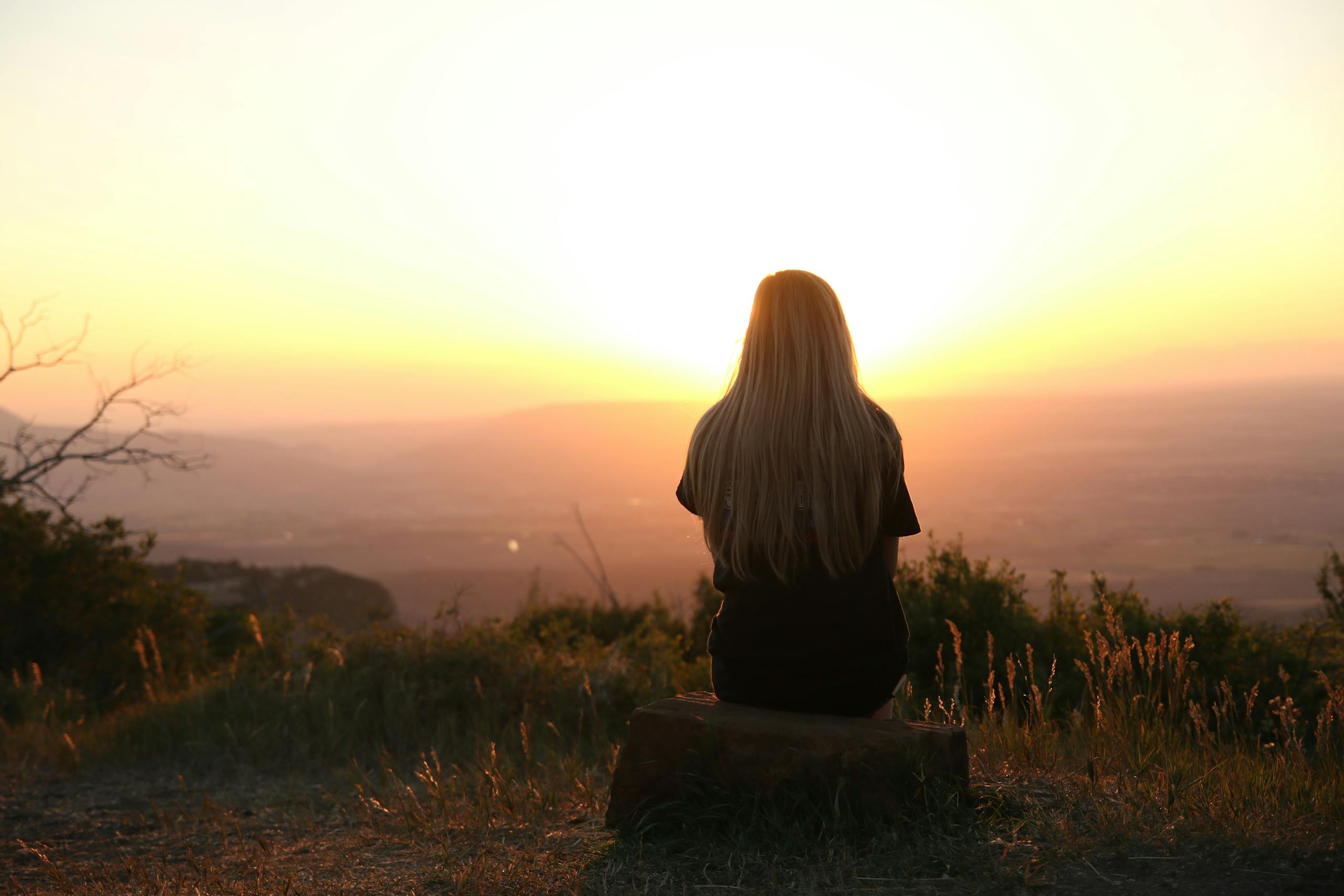 Woman sitting in nature watching sunset over fields in peaceful outdoor scene