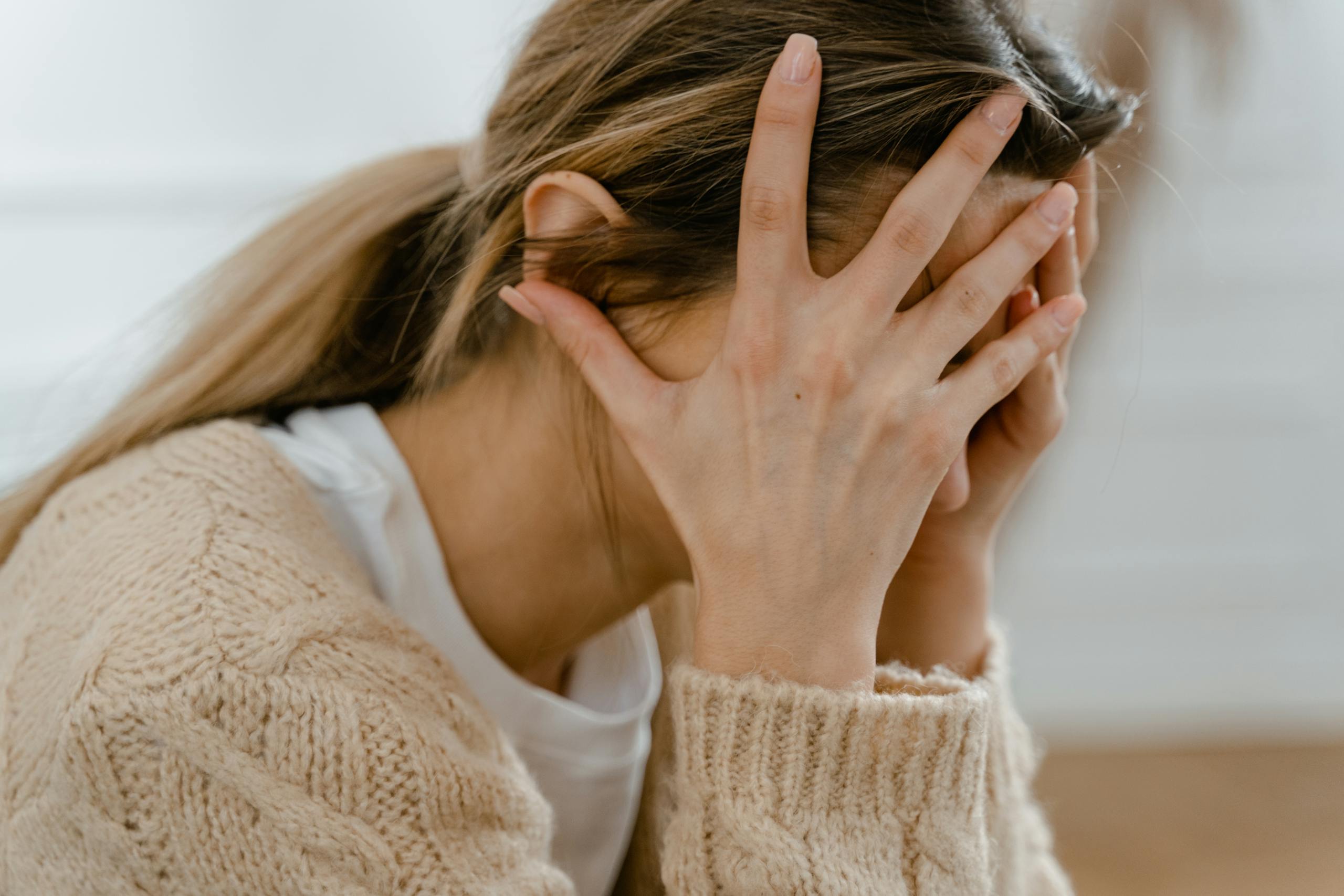 Woman sitting indoors with face covered by hands expressing stress