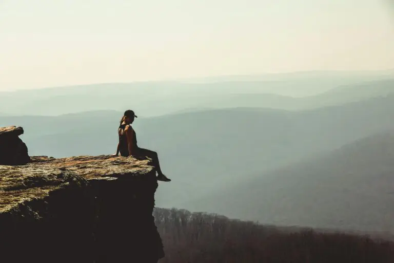 Woman sitting on cliff edge overlooking vast mountain landscape.