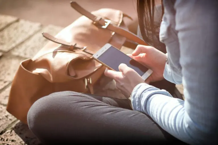 Woman sits with smartphone and brown bag in natural sunlight.