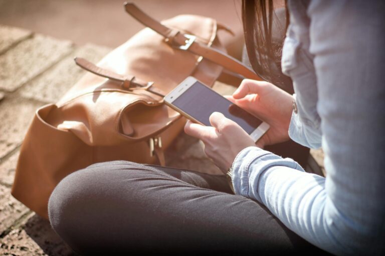 Woman sits with smartphone and brown bag in natural sunlight.