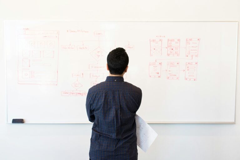 Person studying complex whiteboard diagrams alone, contemplating strategic planning