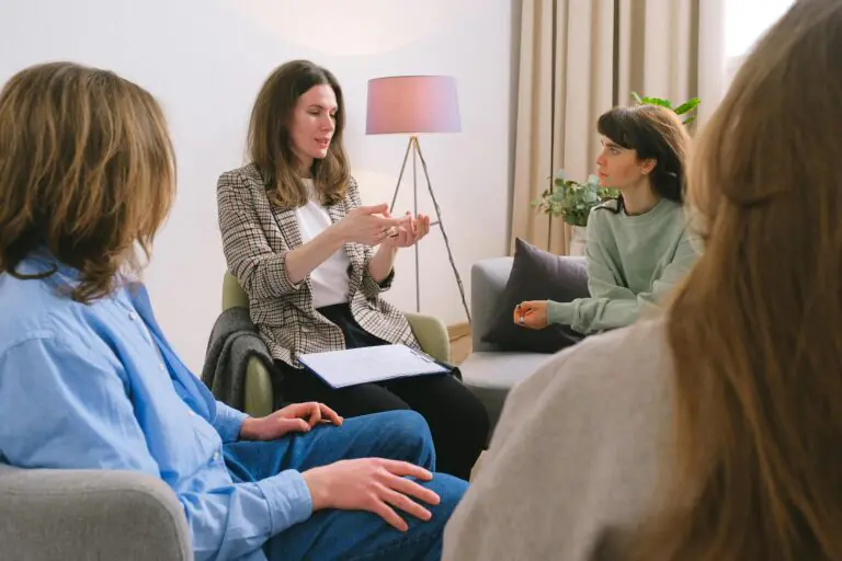 Young female therapist sitting on chair discussing problems with patients during group psychotherapy session