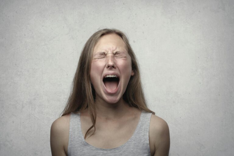 Young woman screaming with emotion showing braces against gray backdrop.